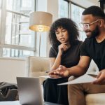 Finance, account and black couple with laptop on sofa doing online banking. Bills, budget and black man and woman with documents, paperwork and computer doing banking, payment and check bank account
