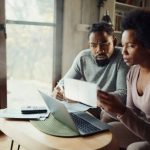 Worried African American couple paying their finances over a computer at home. Focus is on man.